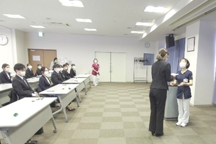 新人看護師が一人ずつ前に出て、看護部長から事例書を渡されている様子