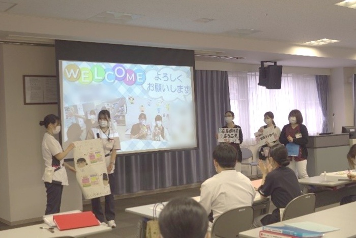 ウェルカムと書かれたスライドの前で5名の看護師がプレゼンをしている