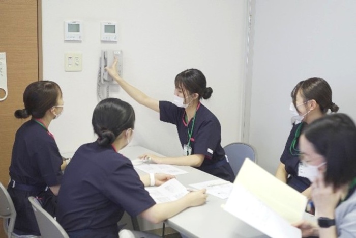 先輩看護師が4名の新人看護師に電話応対の研修をしている。