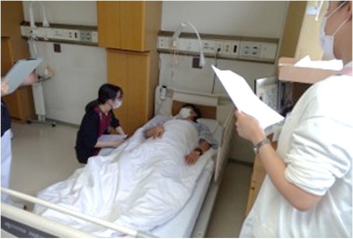 ベッドに横たわる患者さまに新人看護師がしゃがんで話しかけている様子